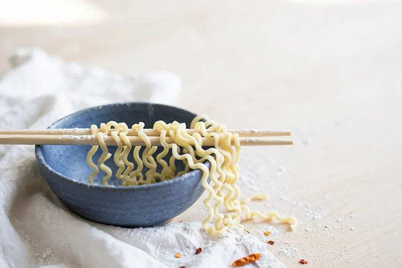 Illustration of fresh ramen noodles resting on the rim of a ceramic bowl